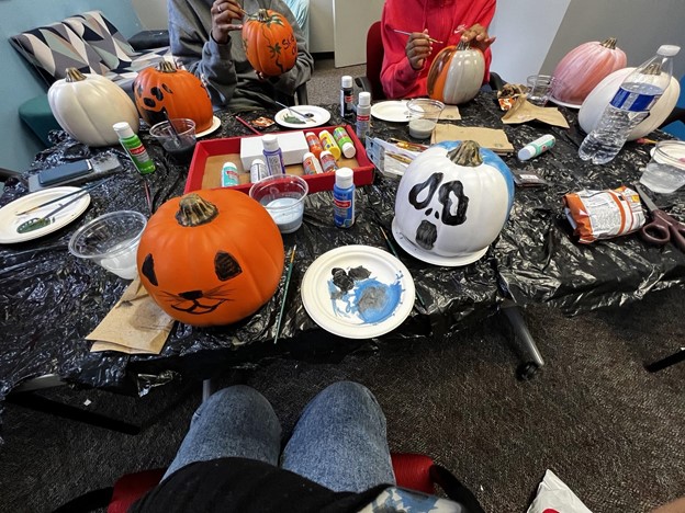 A table with painting supplies, with painted pumpkins on the table as well.