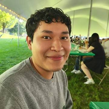Mathew Smiles while sitting at a picnic table under a large tent