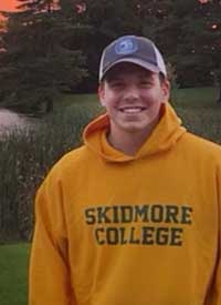 Student wearing a baseball cap yellow skidmore sweatshirt that reads Skidmore College
