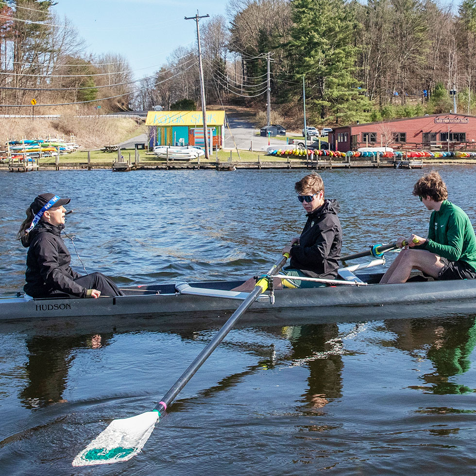 Emma Laquinta ’25 sits on the far end of a scull crew boat in the coxswain position leading the Men's crew team while practicing on Fish Creek