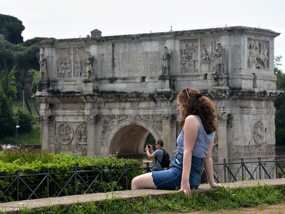 A student sits on a wall overlooking the Arch of Constantine while studying abroad in Rome, Italy.