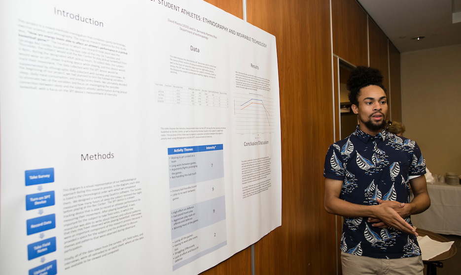 A college student stands before a poster filled with research data and charts