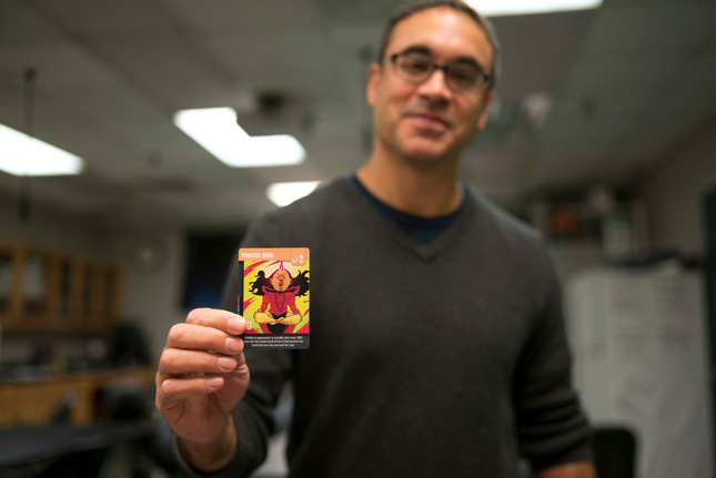 Hassan Lopez, professor at Skidmore, holds up a playing card from his board game