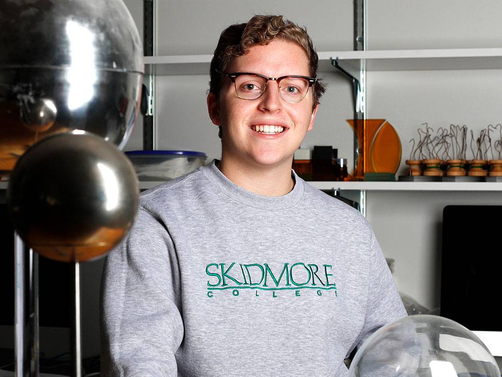 Student poses with silver globes while wearing a Skidmore grey sweatshirt