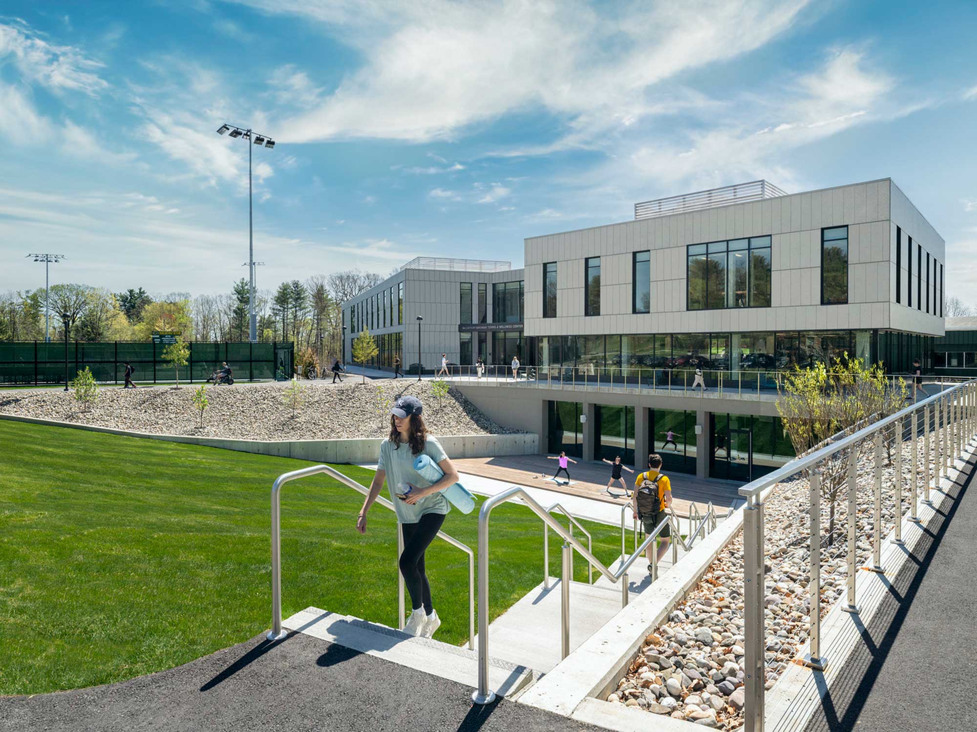 Students walk outside Skidmore’s McCaffery-Wagman Tennis and Wellness Center on a sunny day, with tennis courts and modern campus buildings nearby.