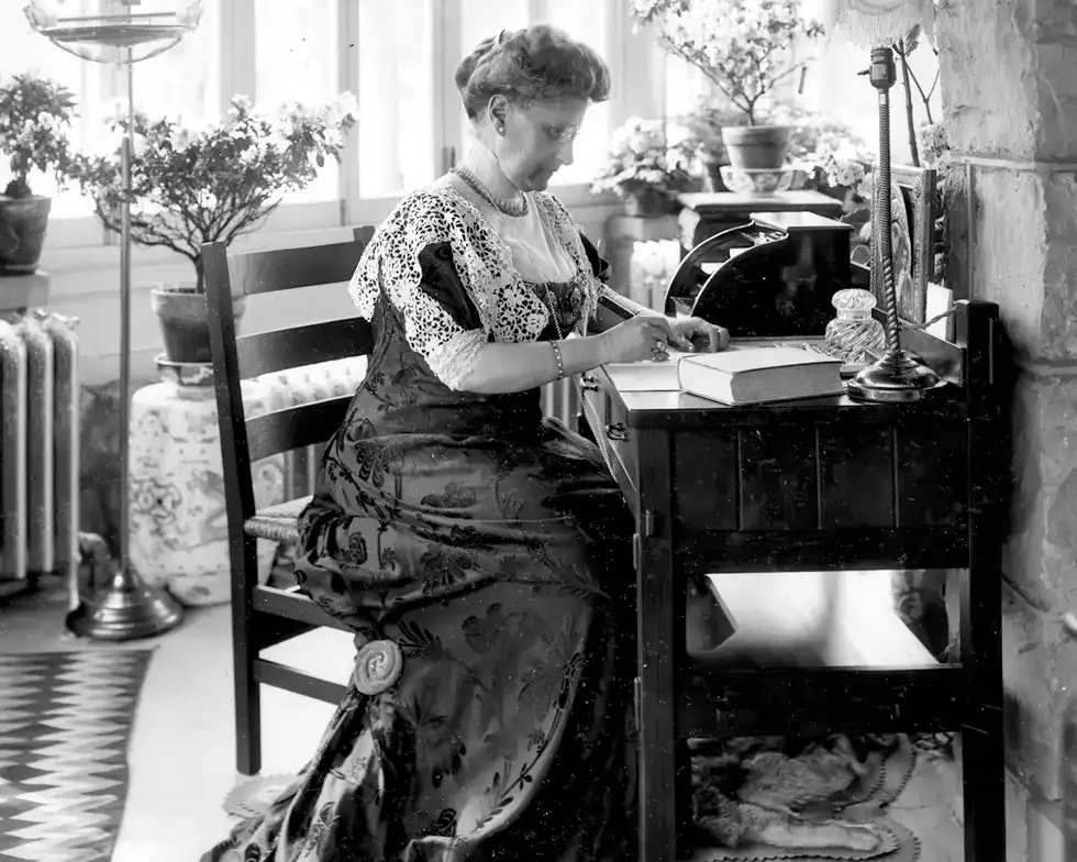 Historic black-and-white photograph of Lucy Skidmore Scribner, founder of Skidmore College, seated on the front steps of a stone building, wearing a long white dress with lace detailing.