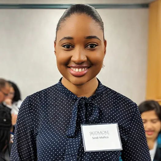 A student in professional clothing smiles into the camera outside of an interview room during a recruiting event.