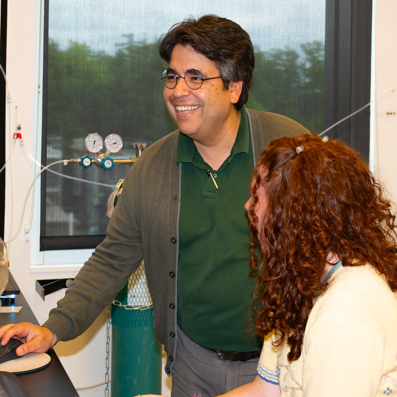 Smiling Skidmore faculty member working with a student in a science lab, reviewing data together on a computer.