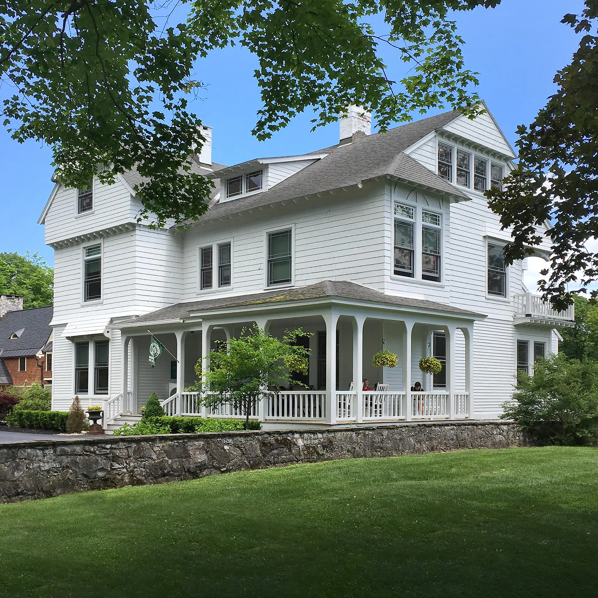 A large white house with a wide front porch and hanging flower baskets serves as the Skidmore College Admissions Office.