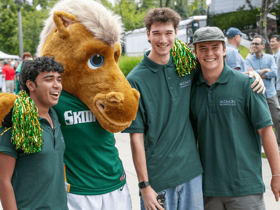 Three students wearing Skidmore swag, joyfully pose with Skids, Skidmore's thoroughbred mascot.