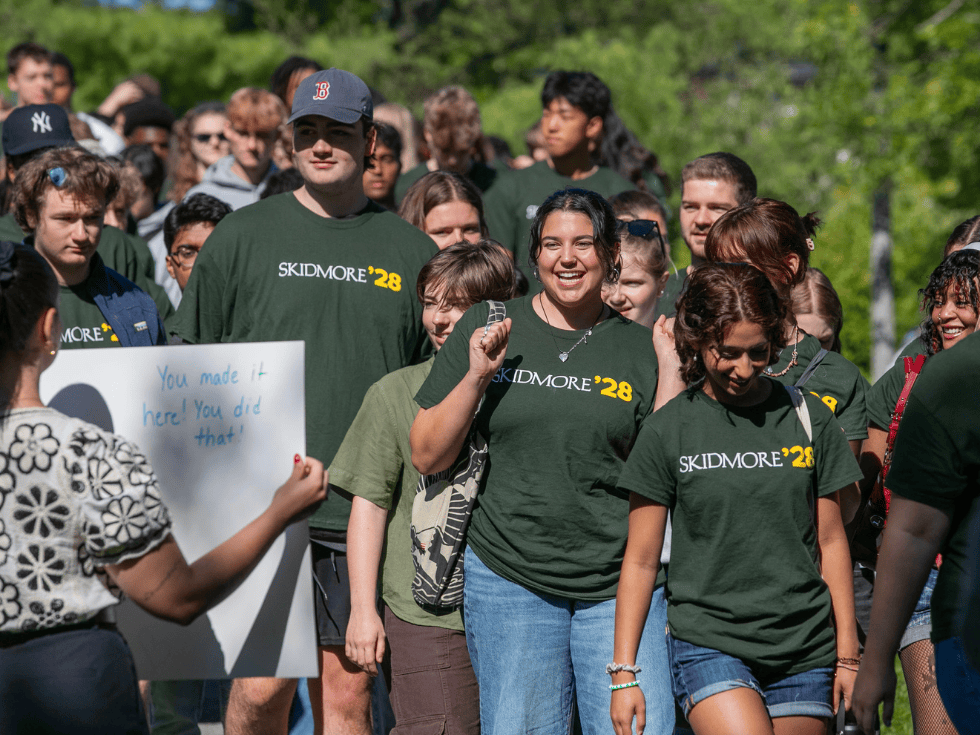 A group of students walking into new student convocation wearing Skidmore shirts and big smiles.