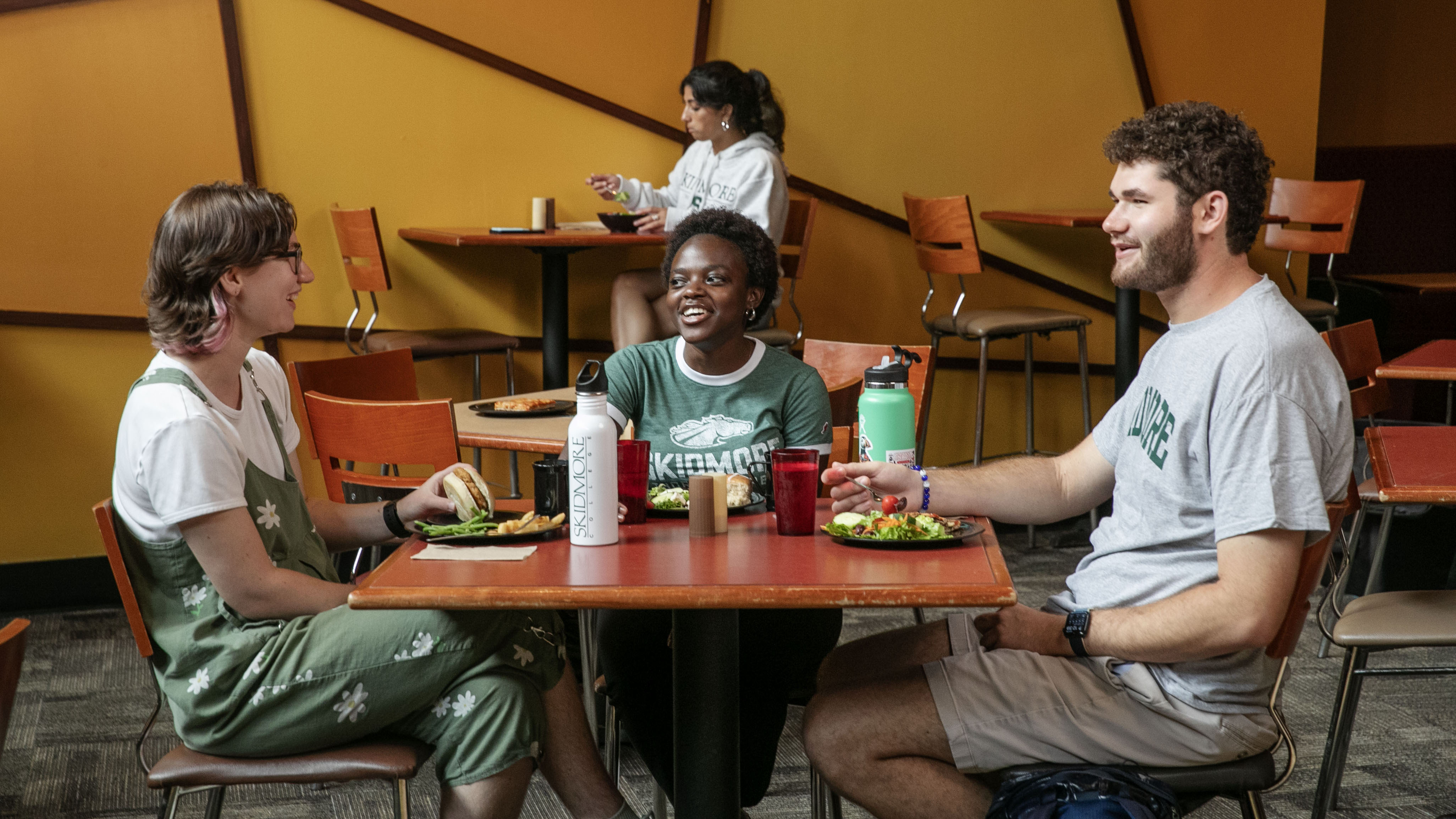 Three students sit at a table in Murray-Aikins Dining Hall, enjoying a meal together