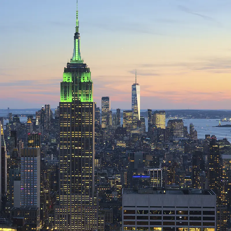 View of the New York City skyline at dusk, with the Empire State Building lit in green and One World Trade Center glowing in the background — showcasing Skidmore’s urban proximity.