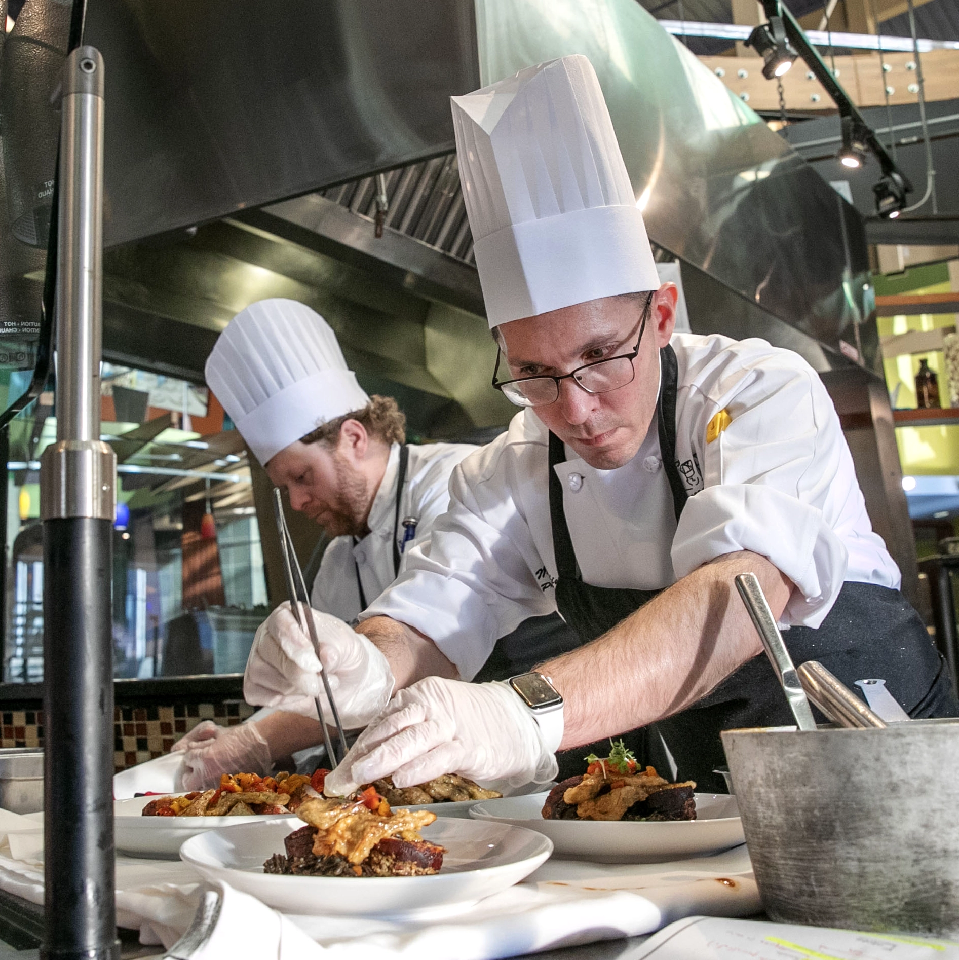 Campus dining chefs in tall white hats carefully plating gourmet meals in a Skidmore College kitchen.