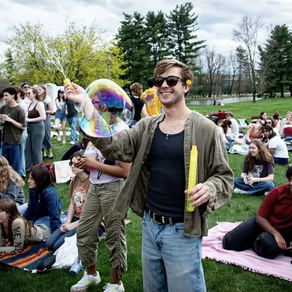 A student in sunglasses plays with a giant bubble wand during Skidmore’s Earth Day celebration on the campus lawn.