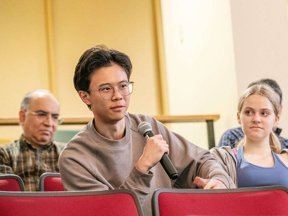 A student sits in an auditorium holding a microphone. 