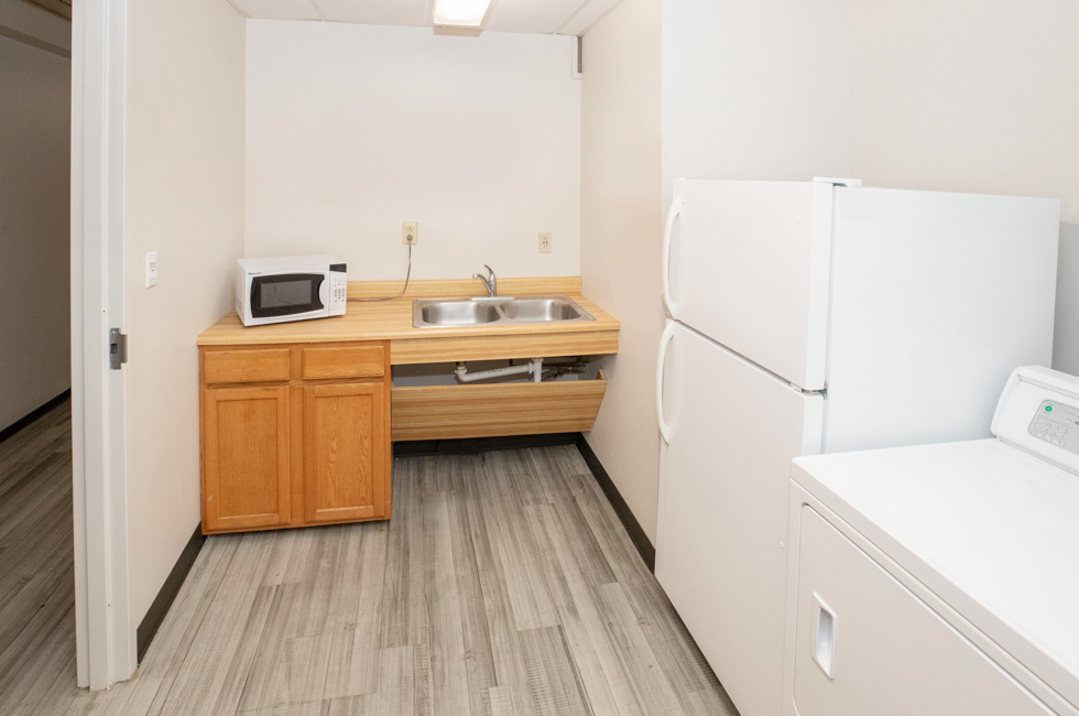 Residence hall kitchen area with a sink, cabinets, microwave, refrigerator, washer, and dryer.