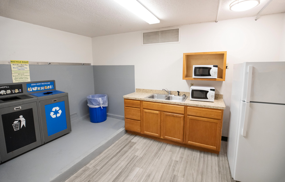 Shared residence hall kitchen with a sink, refrigerator, microwaves, trash, and recycling stations.