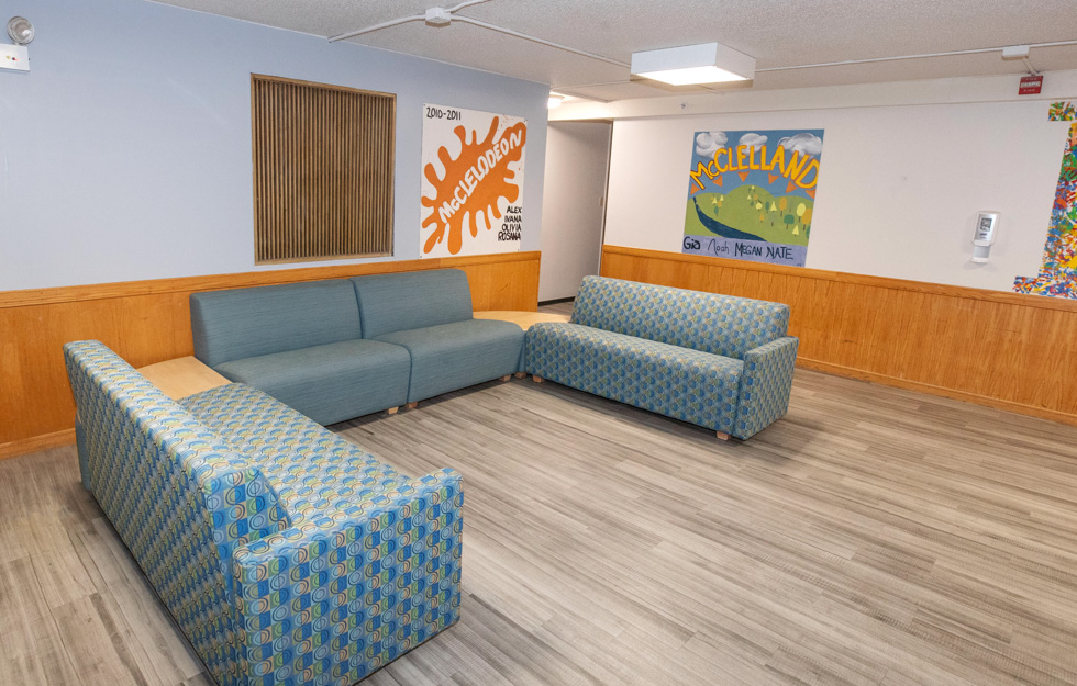 Residence hall lounge with couches, wood paneling, and colorful McClellan wall murals.