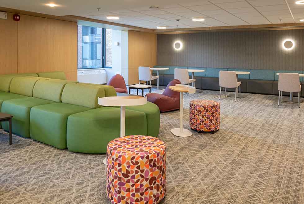 Jonsson residence common lounge with green seating, patterned ottomans, small tables, and booth-style study areas.