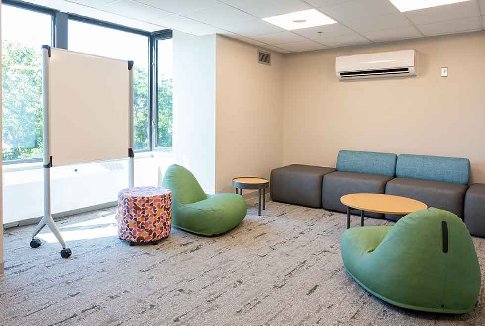 Jonsson residence lounge with a sofa, green lounge chairs, small tables, whiteboard, and large windows.
