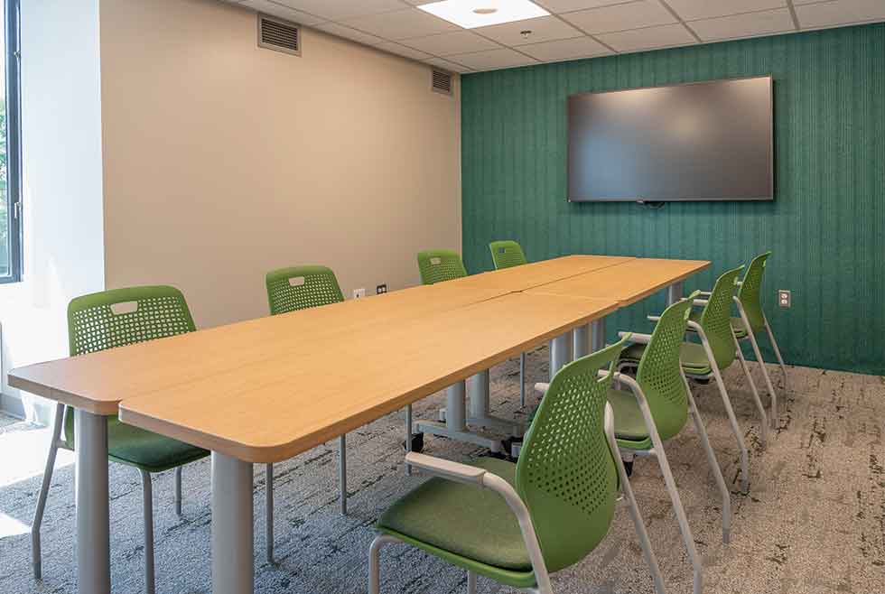 Jonsson residence meeting room with a long table, green chairs, teal accent wall, and wall-mounted display.