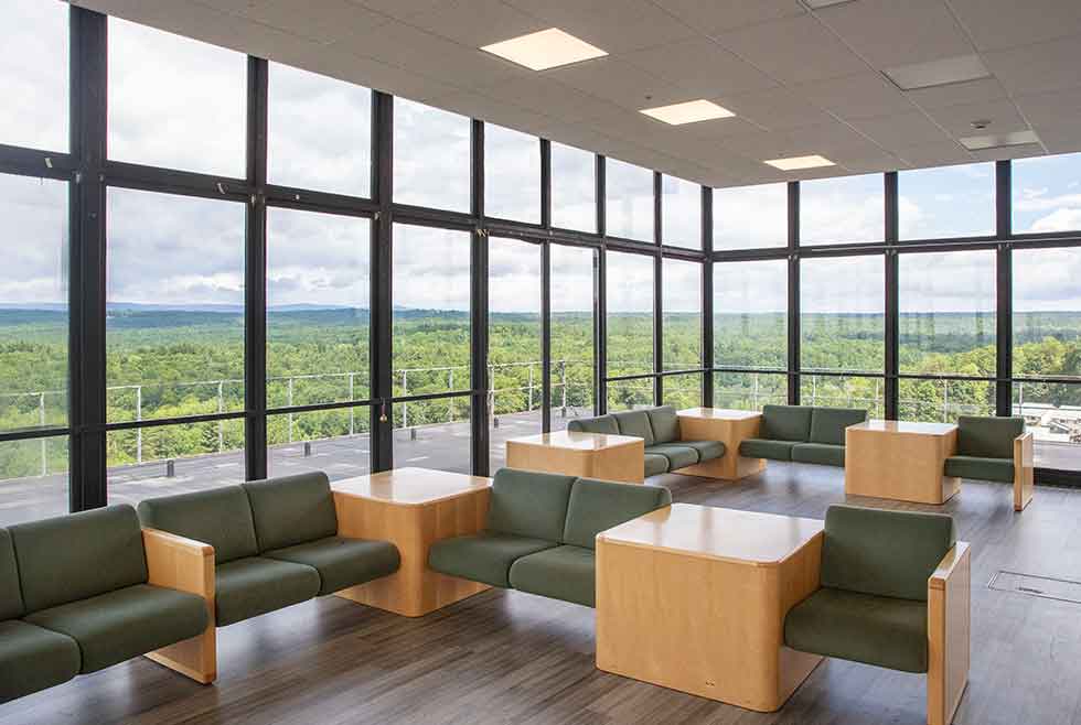 Jonsson residence penthouse lounge with floor-to-ceiling windows, green seating, tables, and panoramic views of the surrounding landscape.