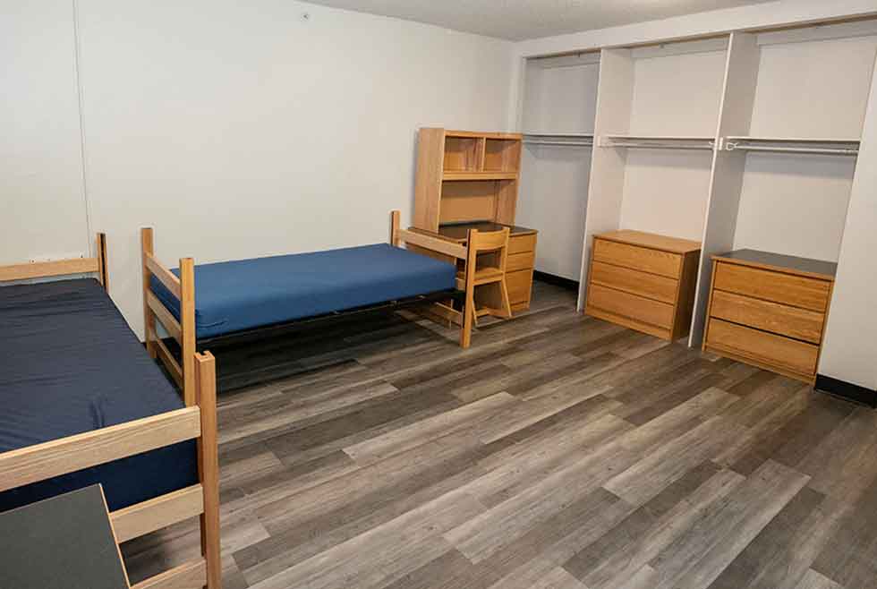 Wait residence double room with two beds, desks, chairs, dressers, shelving, and open closet space.