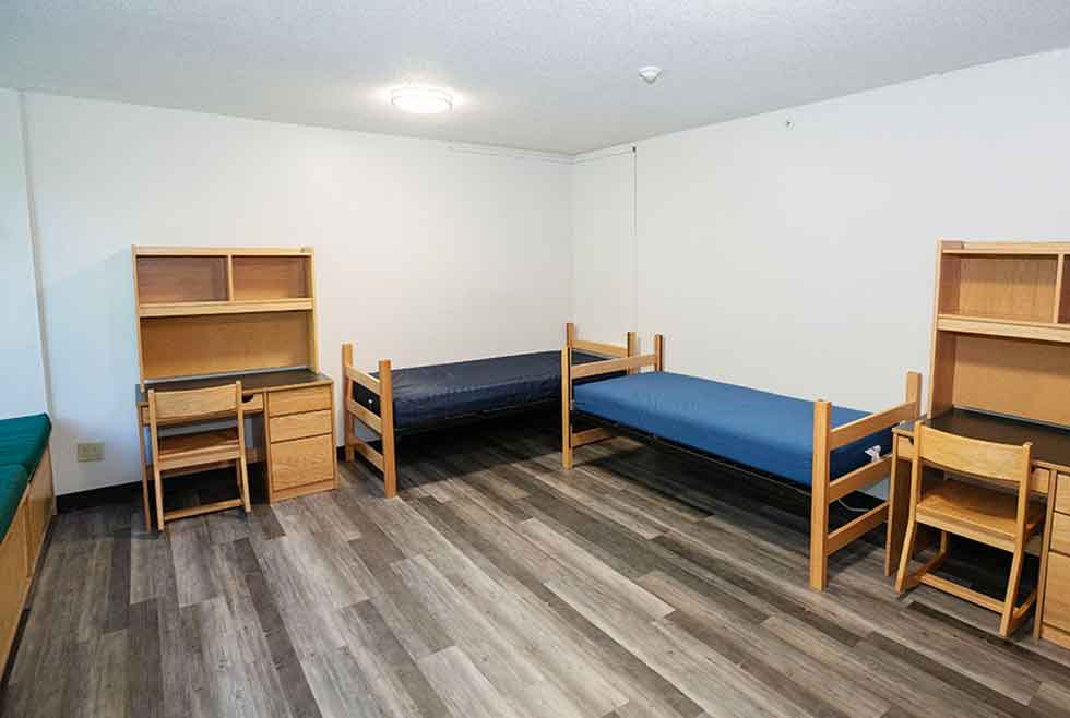 Wait residence double room with two beds, desks, chairs, shelving, and a green-cushioned window seat.