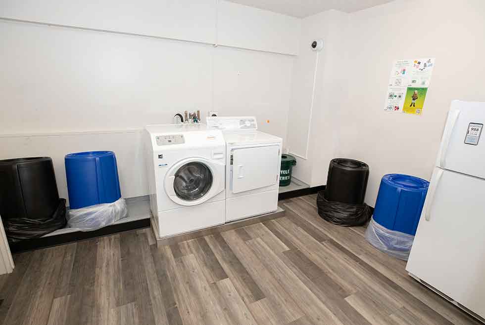 Wait residence laundry room with washer, dryer, refrigerator, and trash and recycling bins.