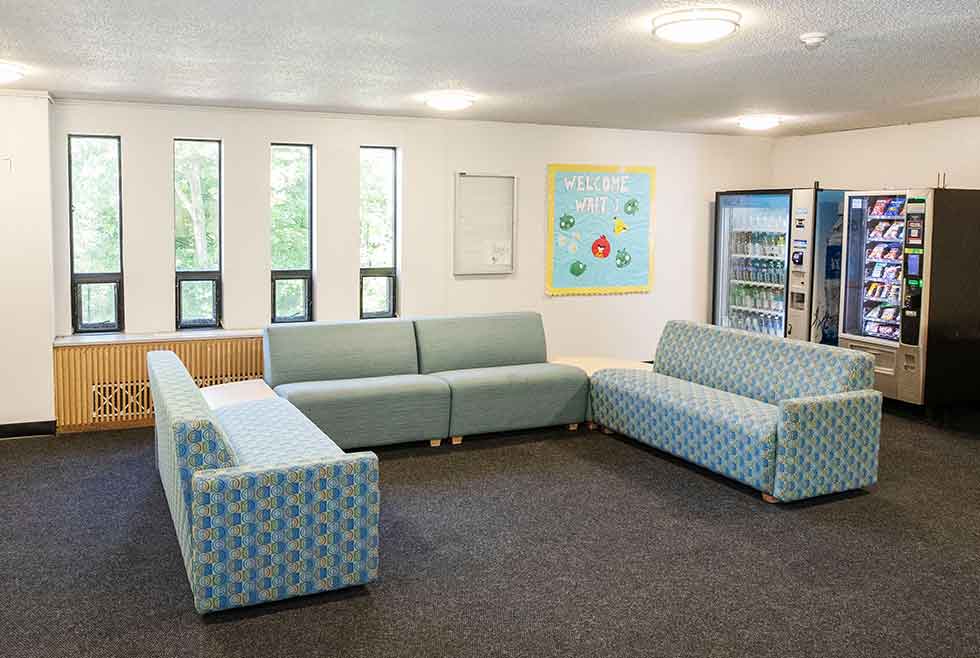 Wait residence lounge with sofas, tall windows, vending machines, and a welcome bulletin board.