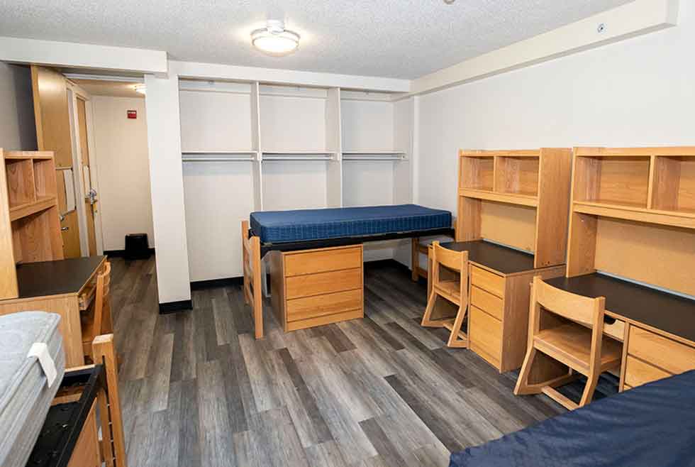 Wait residence triple room with three beds, desks, chairs, shelving, dressers, and open closet space.