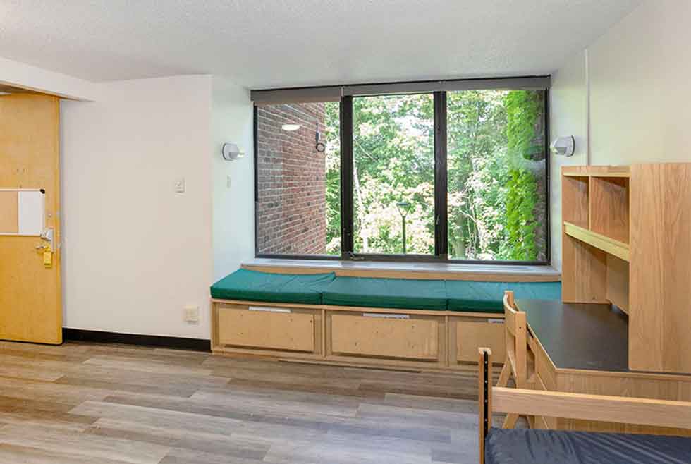 Wait residence room with a green-cushioned window seat, desk, shelving, and part of a bed.