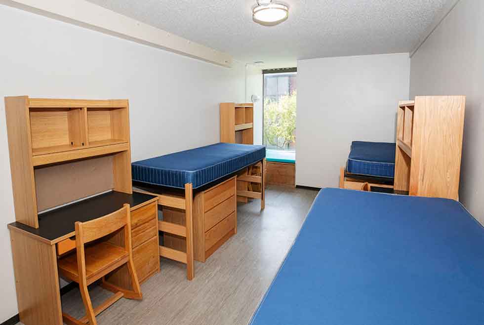 Jonsson residence triple room with three beds, desks, shelves, and a large window.