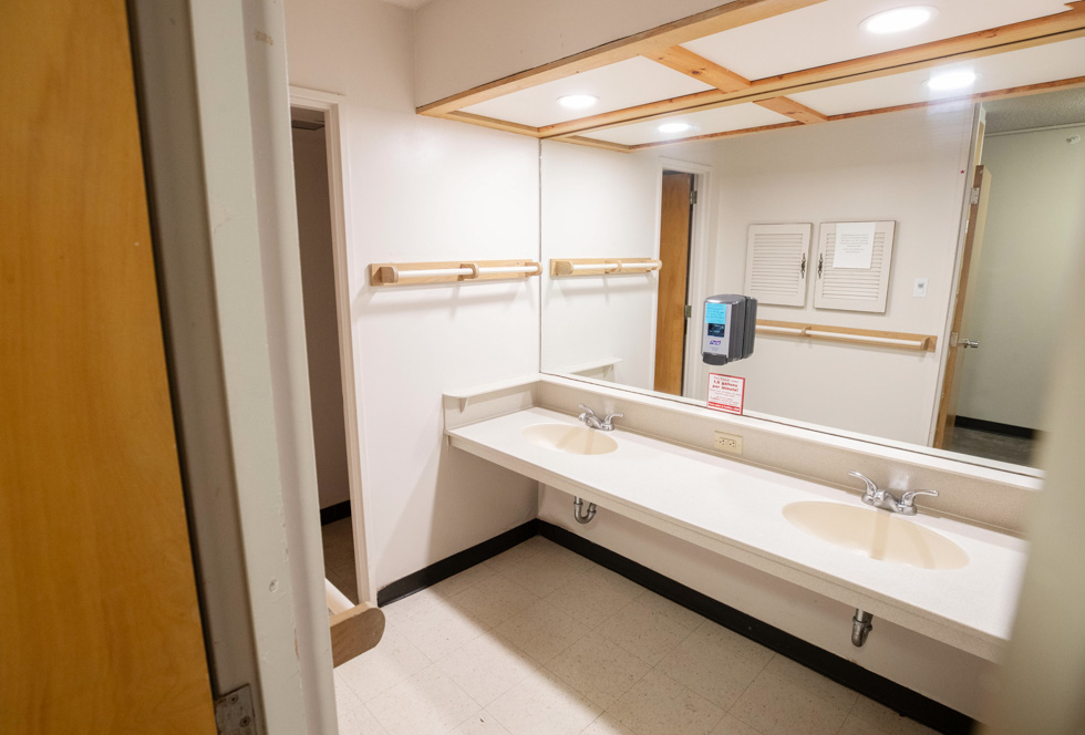 Suite-style residence hall bathroom with two sinks, a large mirror, towel bars, and bright overhead lighting.
