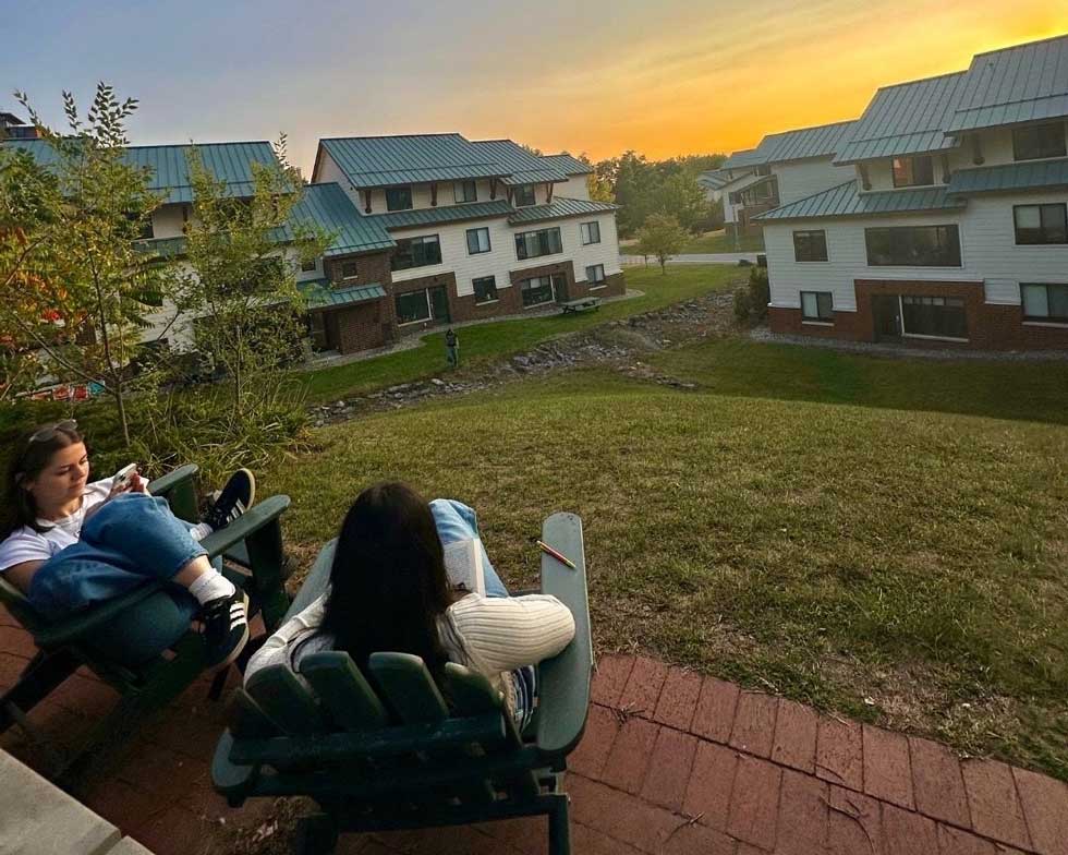 Two students sit in chairs overlooking Skidmore apartment-style residences at sunset.