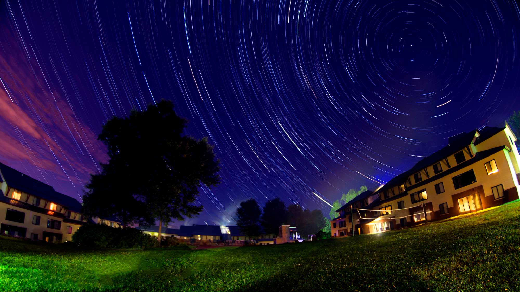 Star trails swirl above Skidmore apartment-style residences during a long-exposure night photograph.