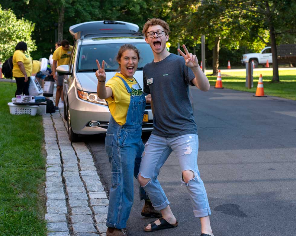 Two smiling resident assistants pose with peace signs during residence hall move-in.