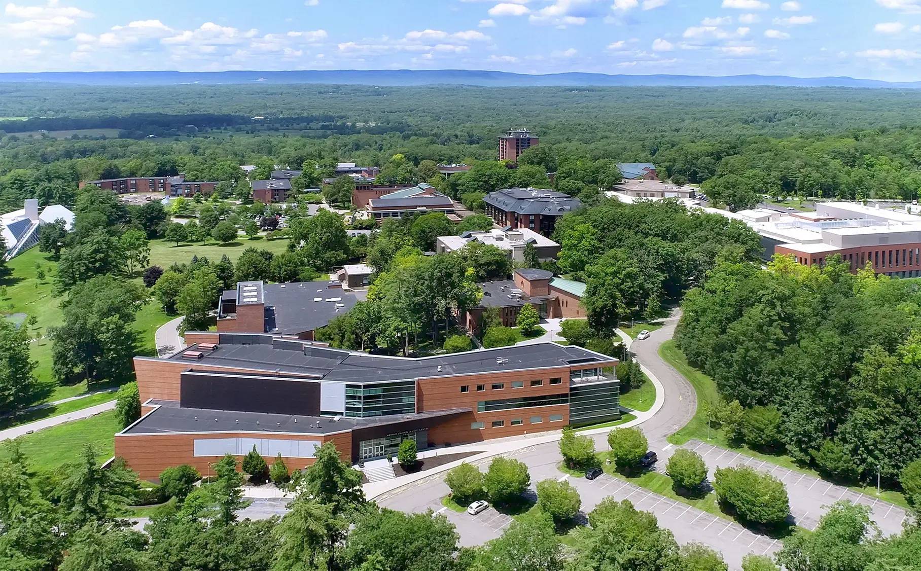 Aerial view of Skidmore College’s scenic campus in Saratoga Springs, New York, showcasing modern academic buildings nestled among expansive green spaces and surrounded by forested hills and mountain ridges in the distance.