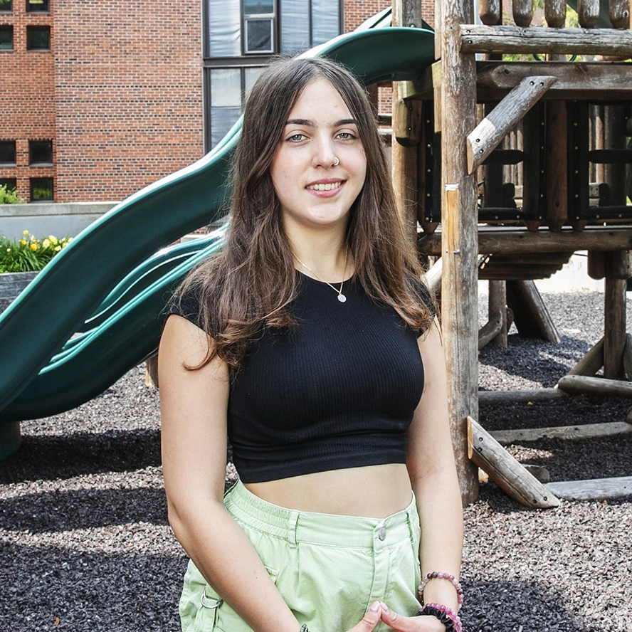 A young college woman stands on a playground and smiles at the camera, a place where she's been conducting developmental psychology.