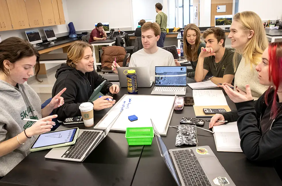 group of Skidmore students gather around a whiteboard and laptops during a collaborative science or math class.