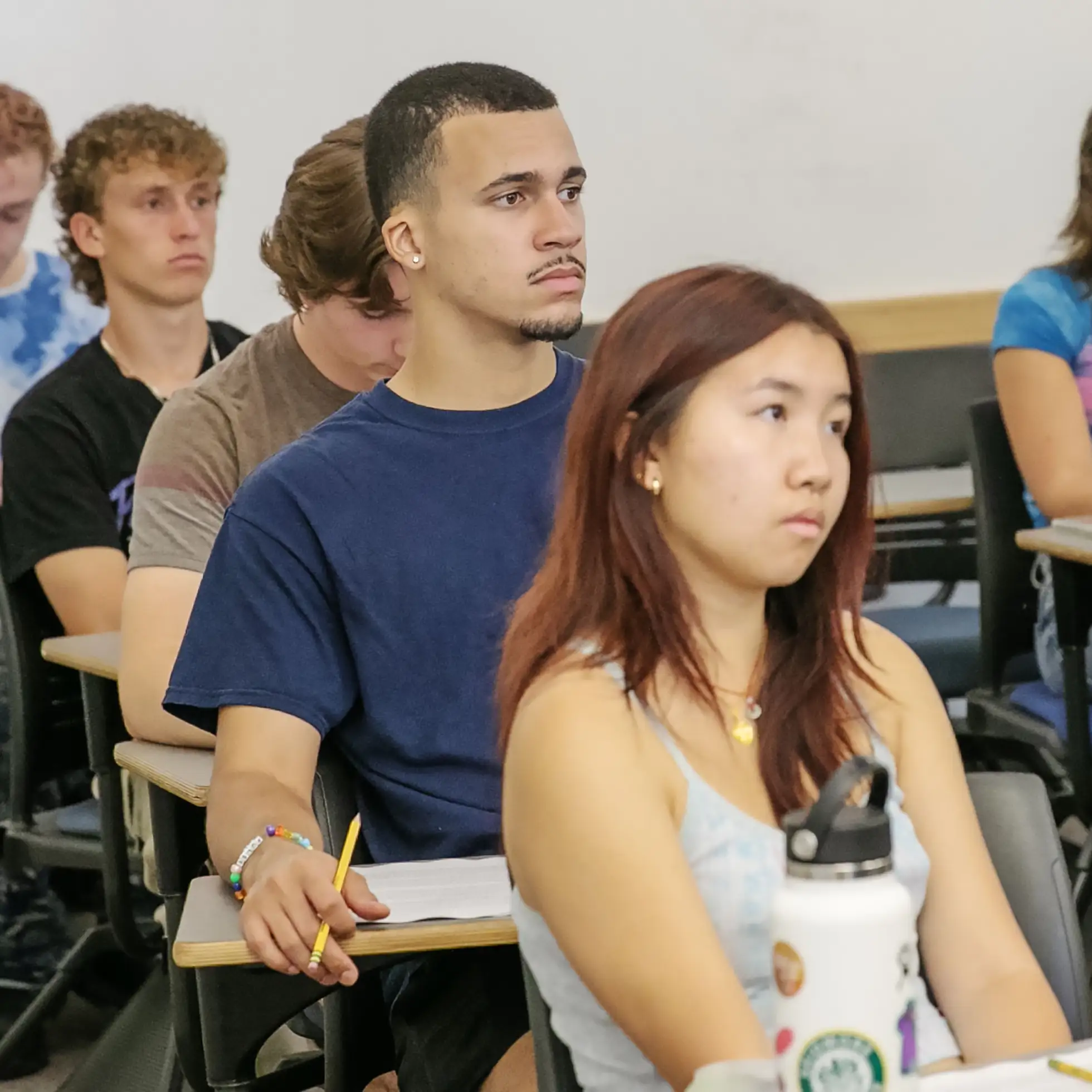 students in a classroom listen attentively to a lecture, notebooks in front of them.