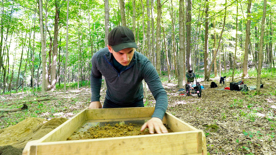 A college student works at an archaeology dig in the woods