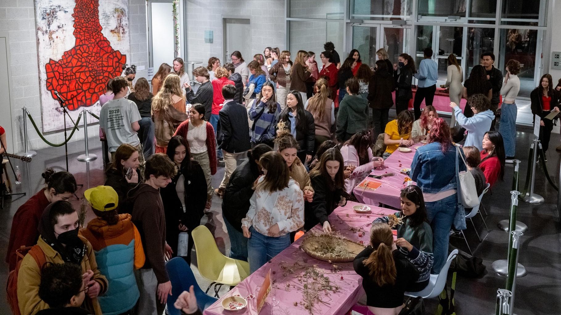 Students gather around pink table-clothed tables to craft and converse.