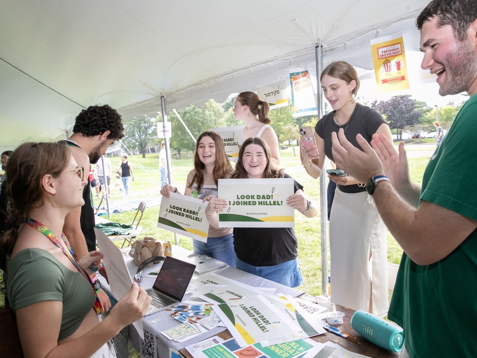 Students at the Hillel booth hold up signs: "Look Dad! I joined Hillel!" and "Look Rabbi! I joined Hillel!"