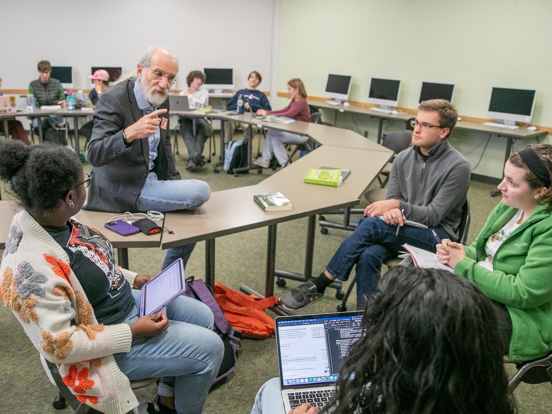Professor Marx sits on a desk and speaks to a small group of Scribner Seminar students.