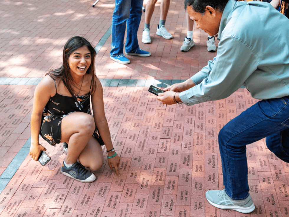 Student smiles with pride as they point to their brick with their name on it.