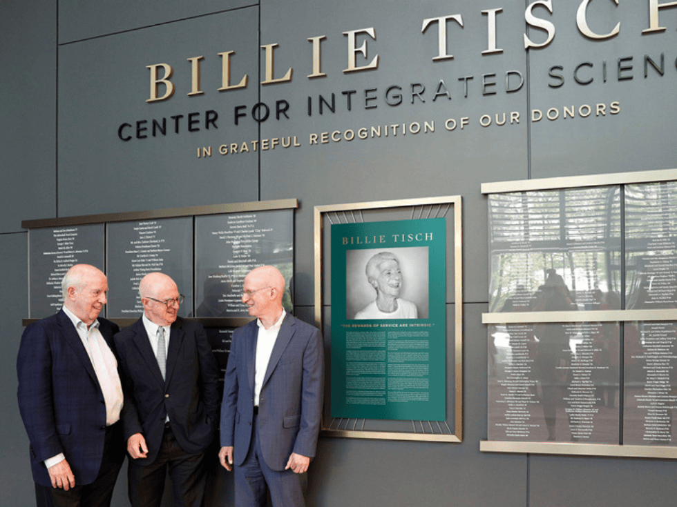 Three older gentleman gather in front of the donor wall in the Billie Tisch Center for Integrated Science.