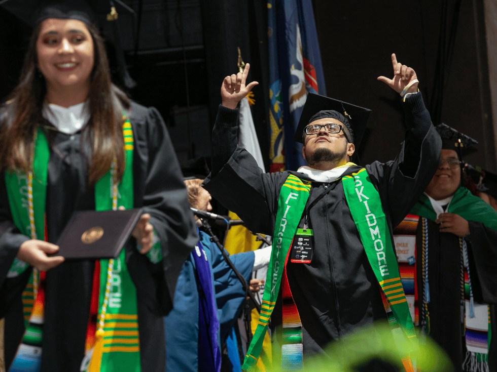 Skidmore student walking across the stage during commencement raising hands in the air in celebration.