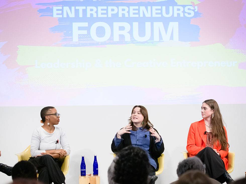Three alums sit on a stage while presenting at the entrepreneur's form in the Tang museum. 